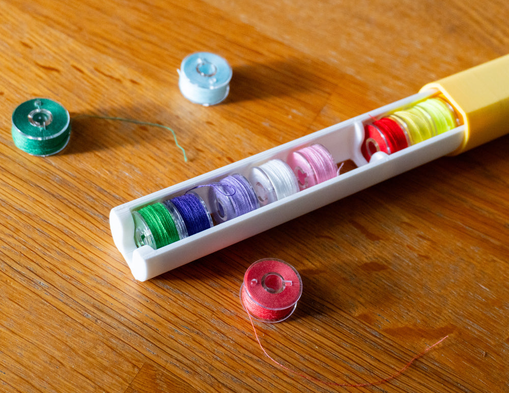 A white 3D-printed bobbin organizer holding rows of colorful sewing bobbins on a wood table