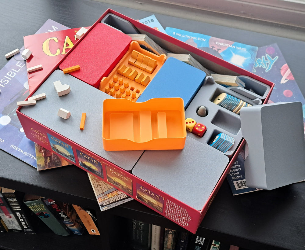A 3D-printed insert tray organizing the pieces of a hex-tile settlement board game