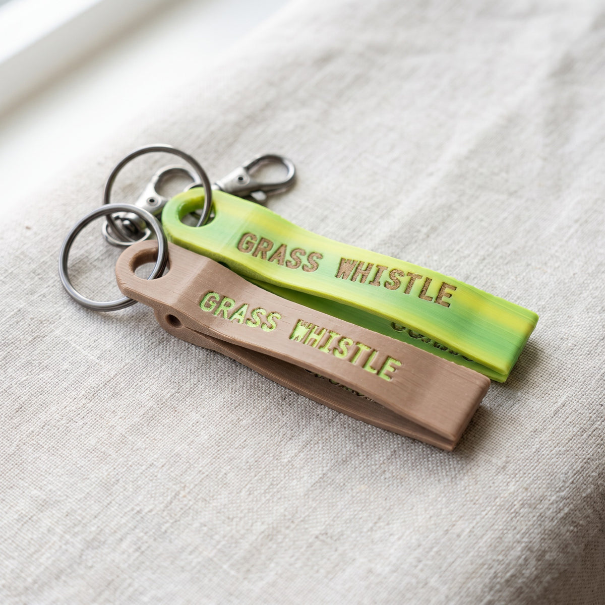 The two colors: lime/yellow gradient with tan letters and tan with lime letters, each on a key ring with a lobster clasp