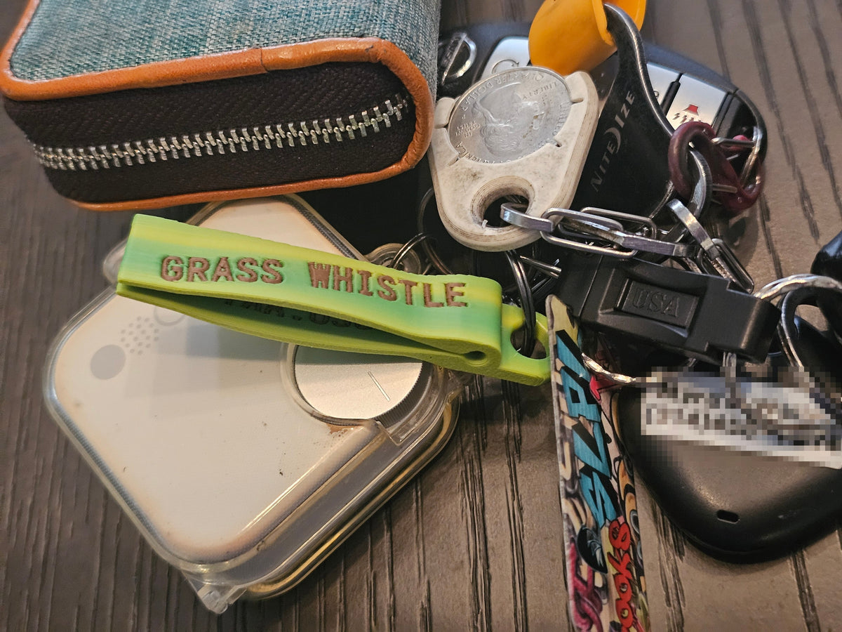 Lime/yellow grass whistle keychain clipped on a set of keys next to a wallet