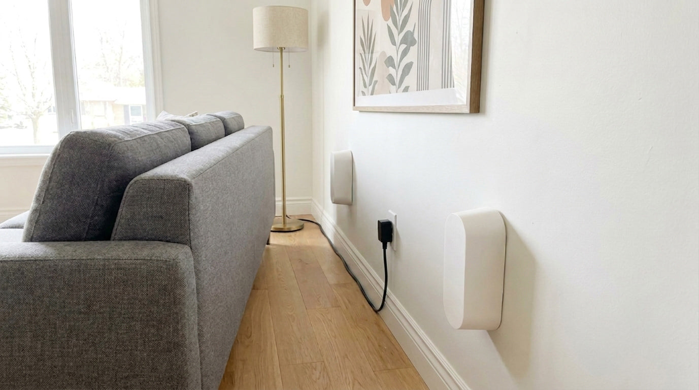 Two white Couch Spacers holding a gray sofa off the wall, with a power cord routed cleanly behind it