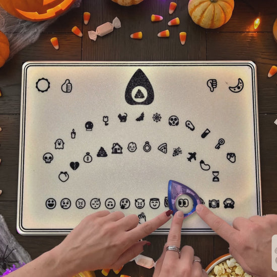 Hands guide the planchette across the emoji spirit board, then fling up in surprise