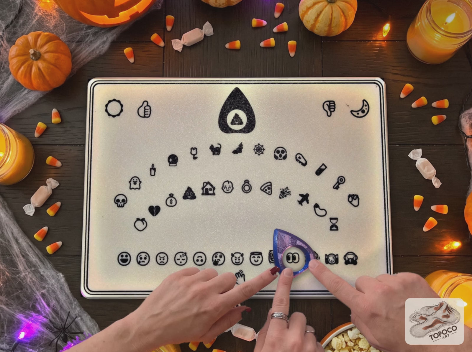 Hands guide the planchette across the emoji spirit board, then fling up in surprise