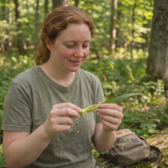 Grass whistle keychain being used in the woods