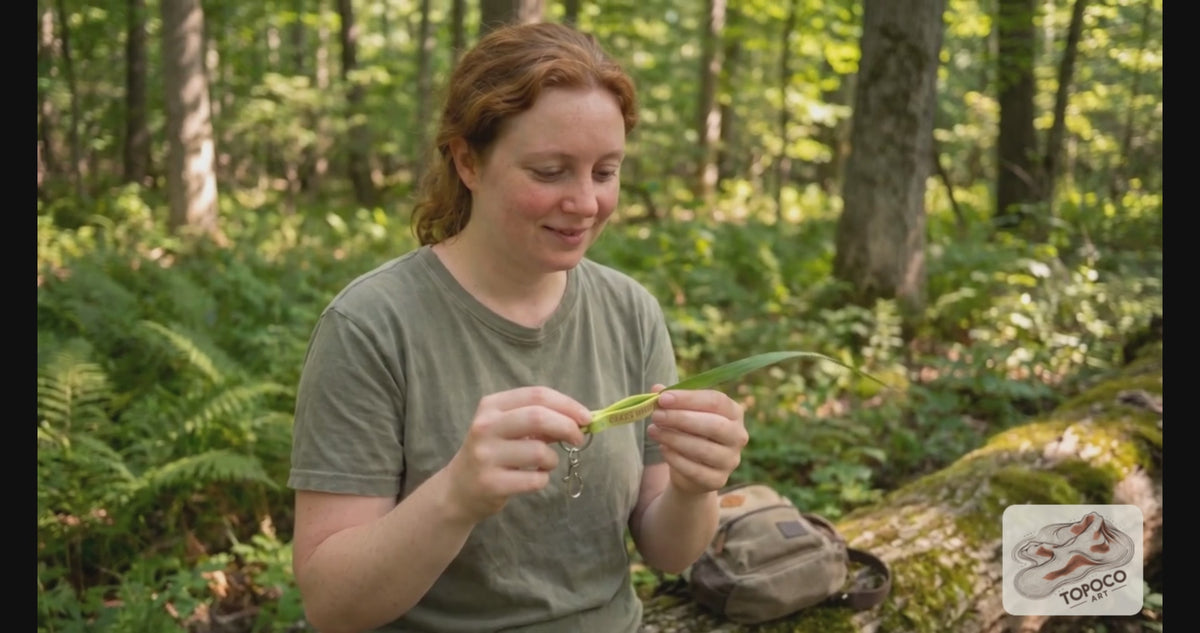 Grass whistle keychain being used in the woods
