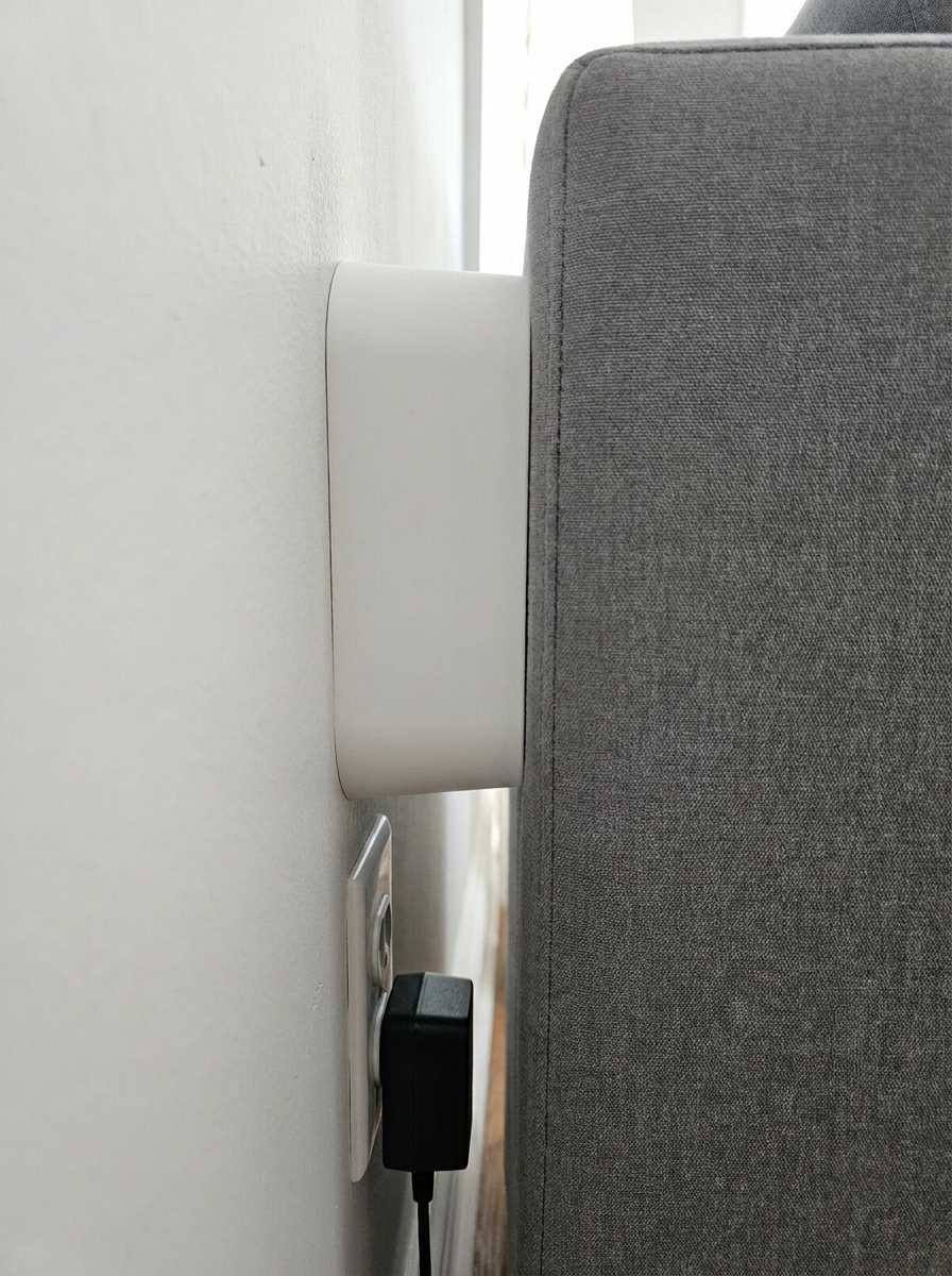 Close-up of a white Couch Spacer between a sofa and the wall, leaving room for a plug in the outlet below
